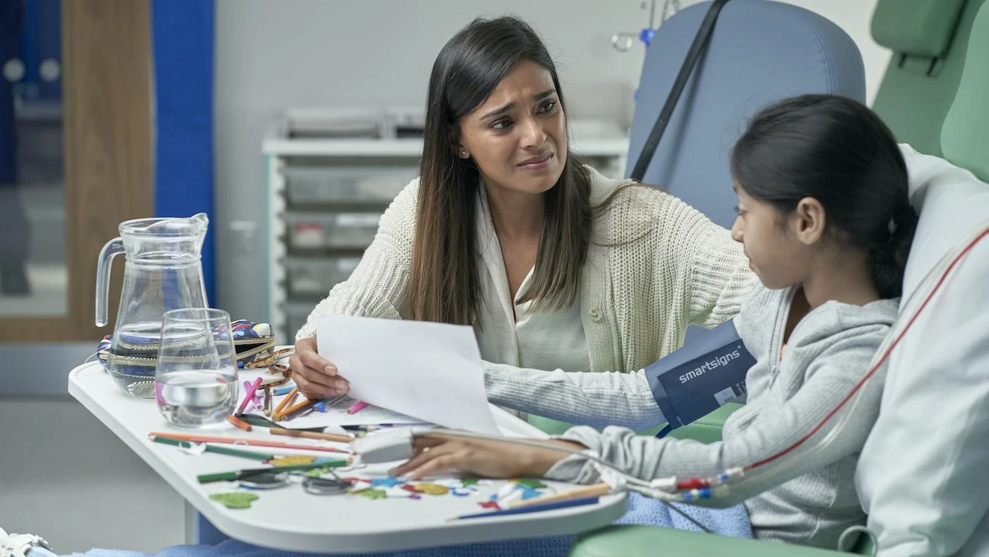 Amara sits with a sad smile on her face with her daughter in the hospital