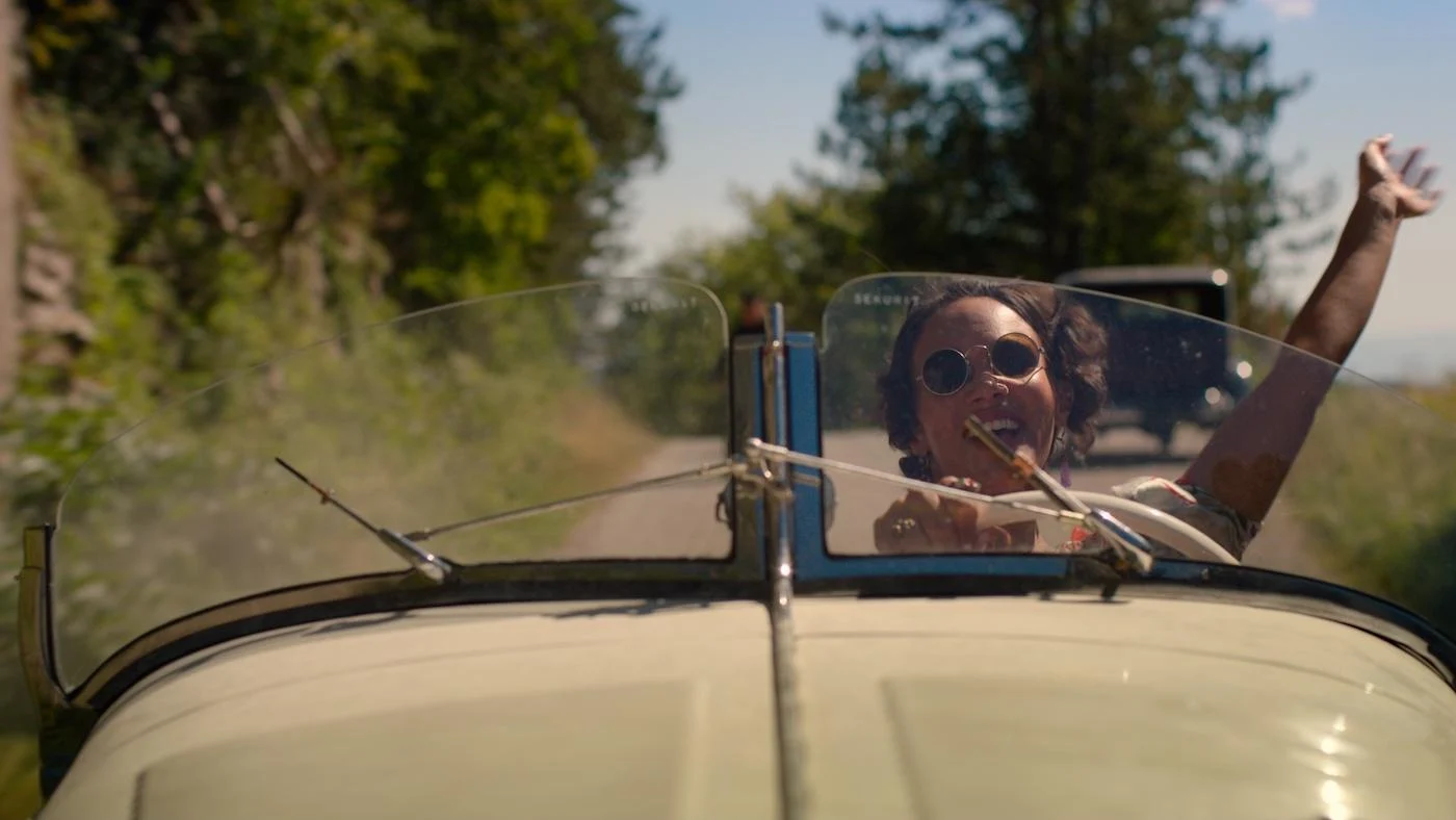 Claudine Pascal waves while driving a convertible